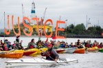 Kayaktivists hold up a series of banners declaring "Climate Justice Now."