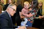 Nikki Dziedzic and her two-year-old son Jude look on as Gov. Jay Inslee props up Judes stuffed penguin while signing HB 1870 on April 17. (Office of the Governor photo)