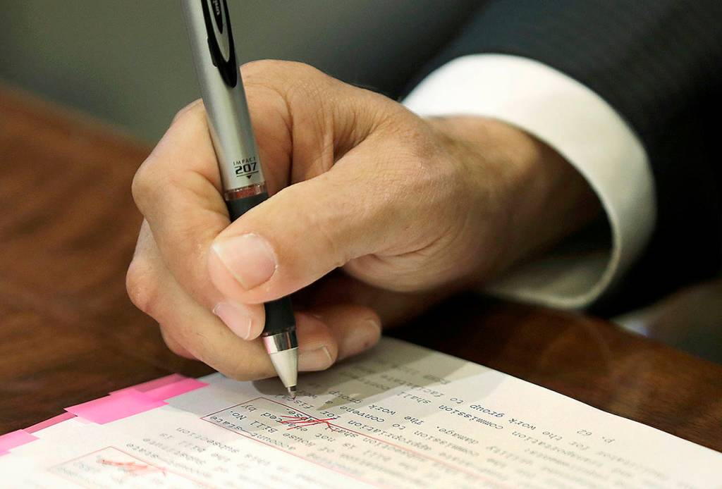 Washington Gov. Jay Inslee uses a red pen to veto sections of the state operating budget Tuesday at the Capitol in Olympia. (AP Photo/Ted S. Warren)