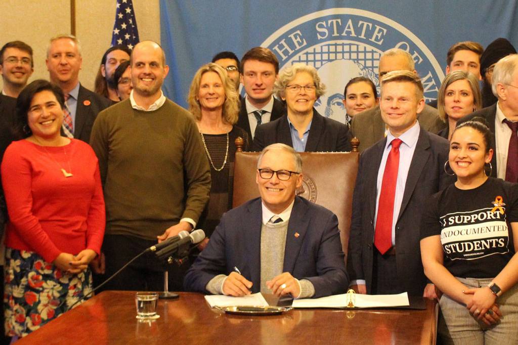 Gov. Jay Inslee signs the first bill of the 2020 legislative session into law. On the right stands the bills primary sponsor, Sen. Jamie Pedersen, D-Seattle, who is wearing a red tie. Photo by Cameron Sheppard, WNPA News Service