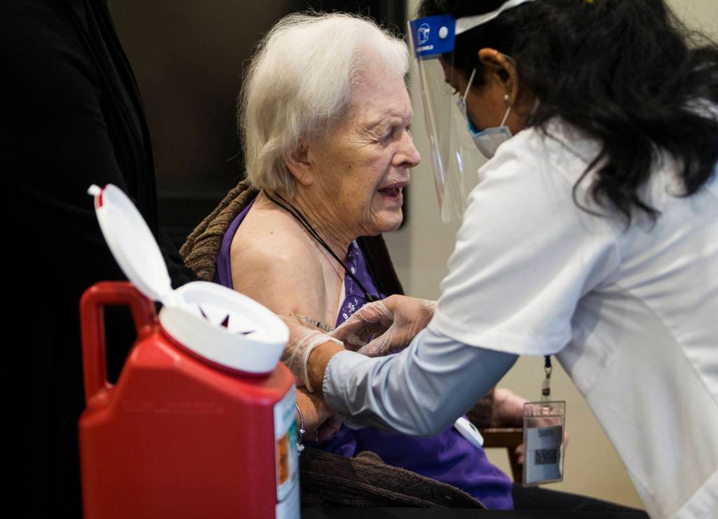 Jackie Hoernor, a resident at South Pointe Assisted Living, winces as she gets her Pfizer COVID-19 vaccination during a Walgreens Vaccine Clinic at South Pointe on Feb. 12 in Everett. (Olivia Vanni / The Herald)